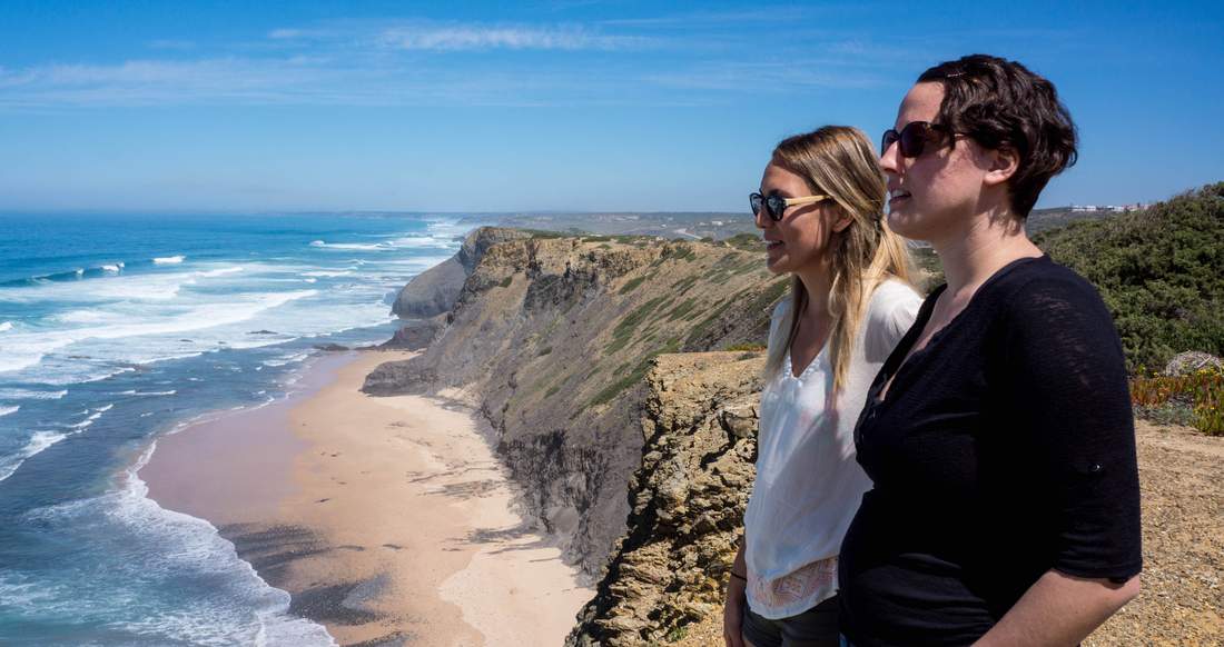 Algarve Portugal Two girls lookout from the top of a large cliff at a beautiful beach and open ocean