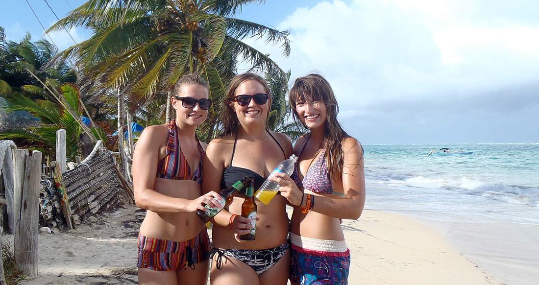 Beach Corn Island Nicaragua Three girls cheers drinks while standing on a white sand beach in colourful bathings suites