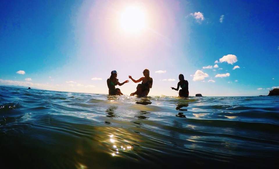 Beach Nicaragua Three women sit on the shoulders of three men in the ocean with a warm sun glow in the background