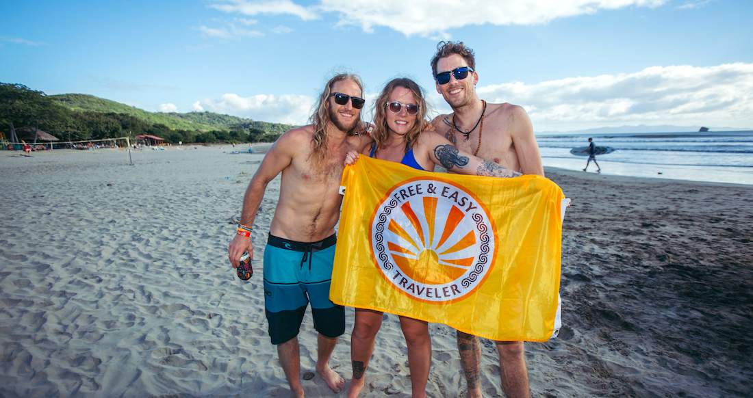 Beach Nicaragua A girl and two guys pose on a beach holding a bright yellow flag as a s surfer walks in the distance