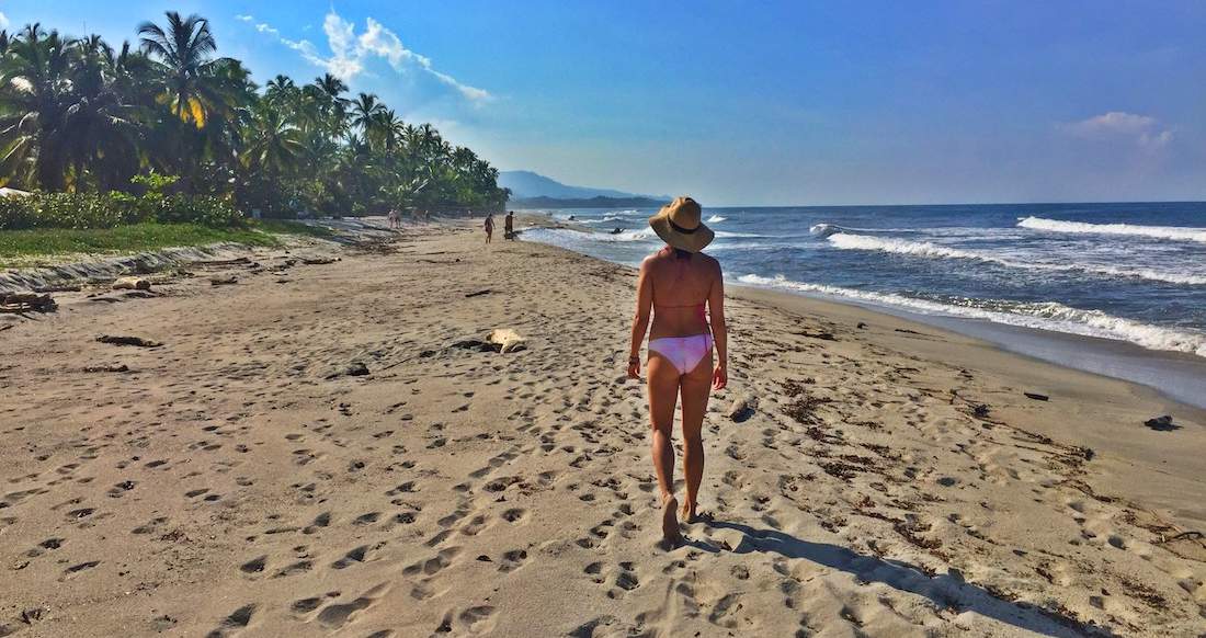 Beaches Colombia A women in a pink bikini and sun hat walks along a palm tree lined beach