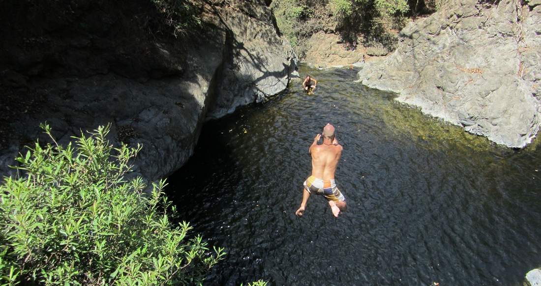 Cliff Jumping Costa Rica A man jumps from a cliff to a natural pool as his friend watches from below