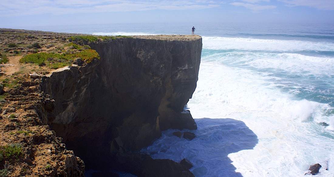 Cliff Portugal Person stands at edge of large cliff overlooking waves on the ocean
