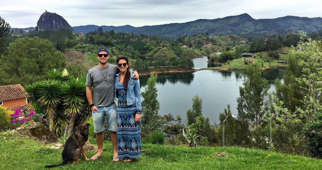 Guatape Lake Colombia A couple stands with a dog in front of a beautiful lake surrounded by rolling green hills
