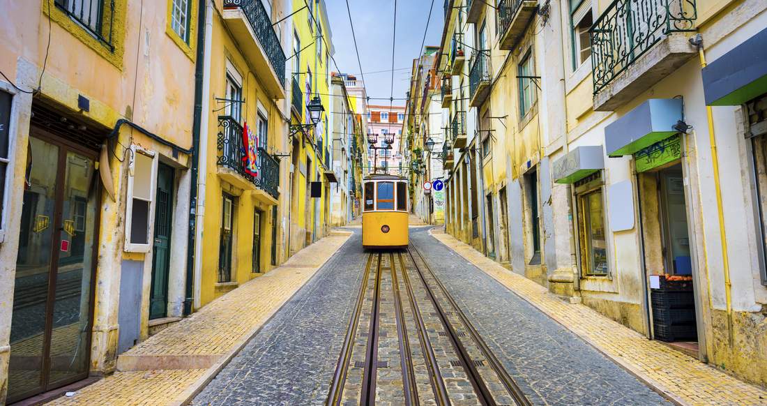 Streetcar Lisbon A Streetcar drives down a narrow lane between cobblestone and colourful buildings