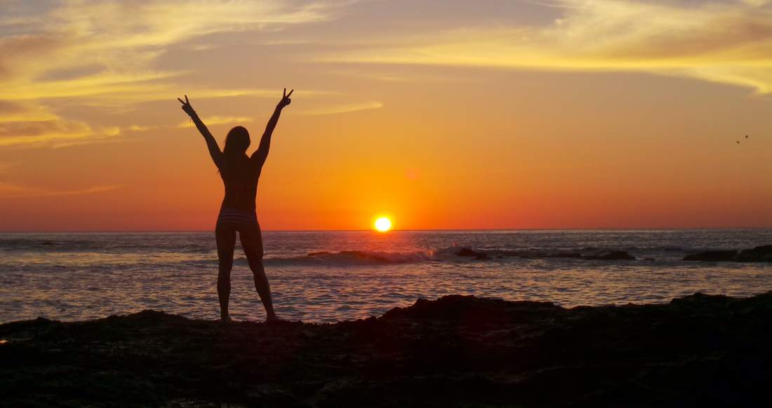 Sunset Beach A Silhouette of a girl on a beach stretching out her arms giving the peace sign at sunset