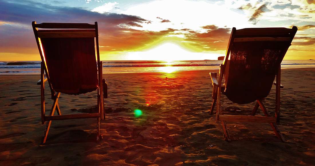 Sunset Nicaragua Two empty beach chairs stand on a quite beach while the sunsets over the ocean creating a deep orange sky