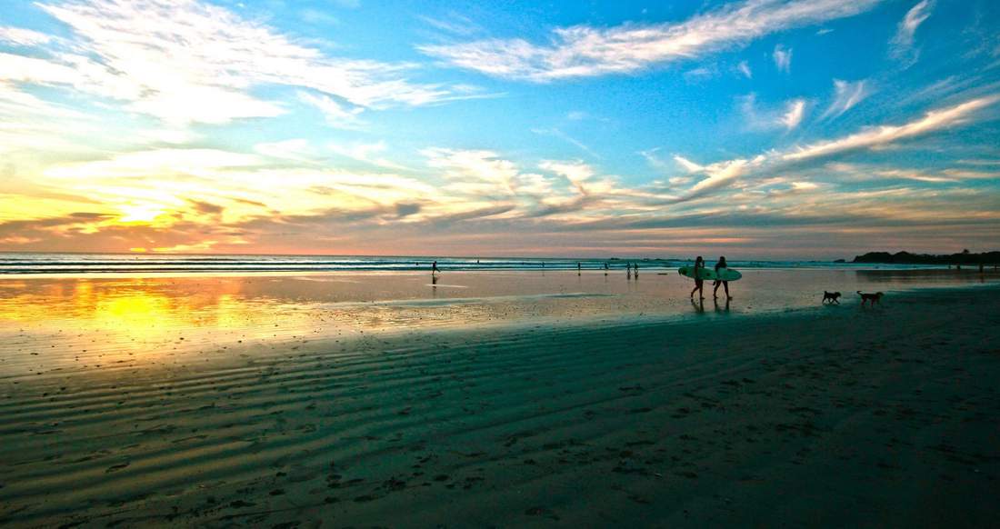 Sunset Surfing Costa Rica Surfers walk along an expansive beach at sunset