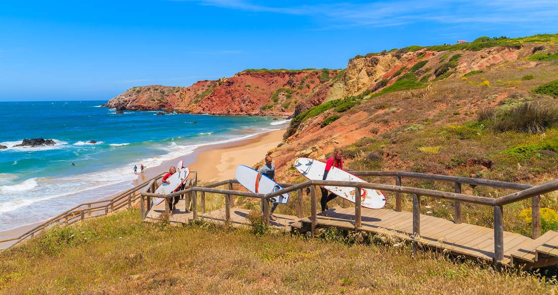 Surfing Algarve A group of people carry surfboards up a wooden staircase from a beautiful beach