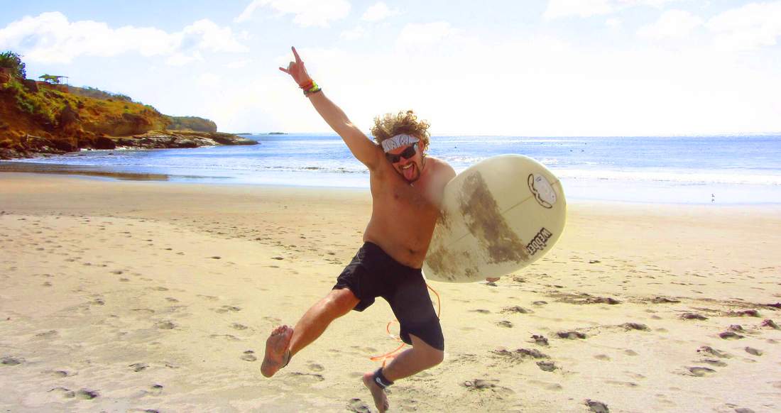 Surfing Nicaragua A man wearing a bandana jumps up in the air with his surf board