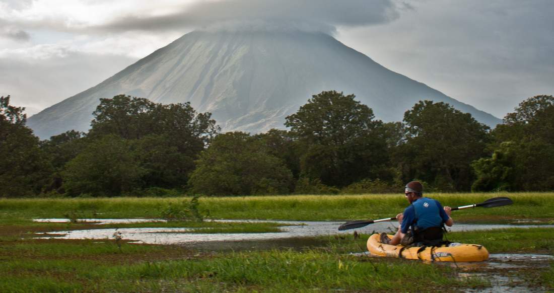 Volcano Nicaragua A man Kayaks through a marshy river with a large Volcano in the background