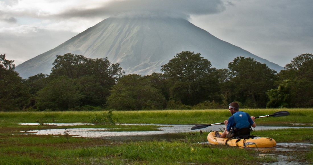Volcano Nicaragua A man Kayaks through a marshy river with a large Volcano in the background