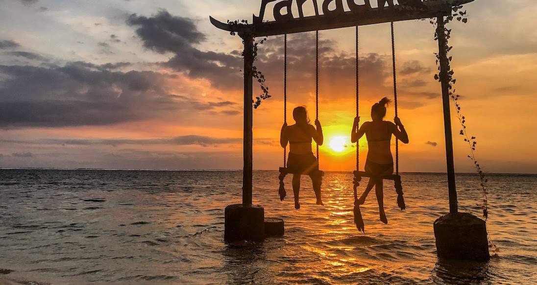 pandawa swing sunset two girls on swings in the ocean while the sun sets in Indonesia