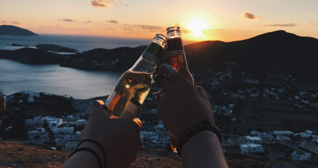 Cheers Two people clinking their beer bottles as the sun sets in Ios Greece