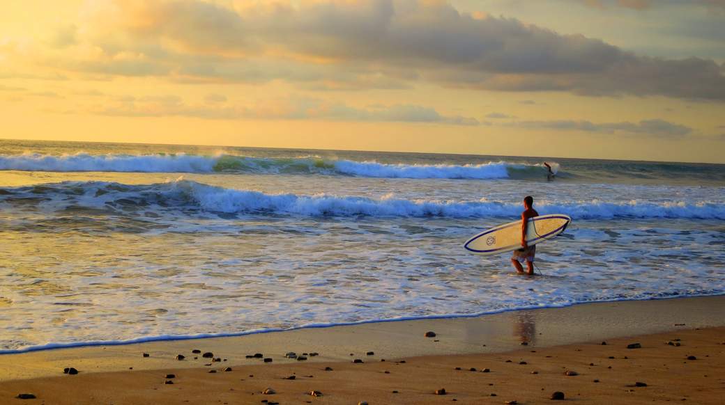 Sunset surfing A dude standing on the beach with his surfboard as the sun sets in Costa Rica