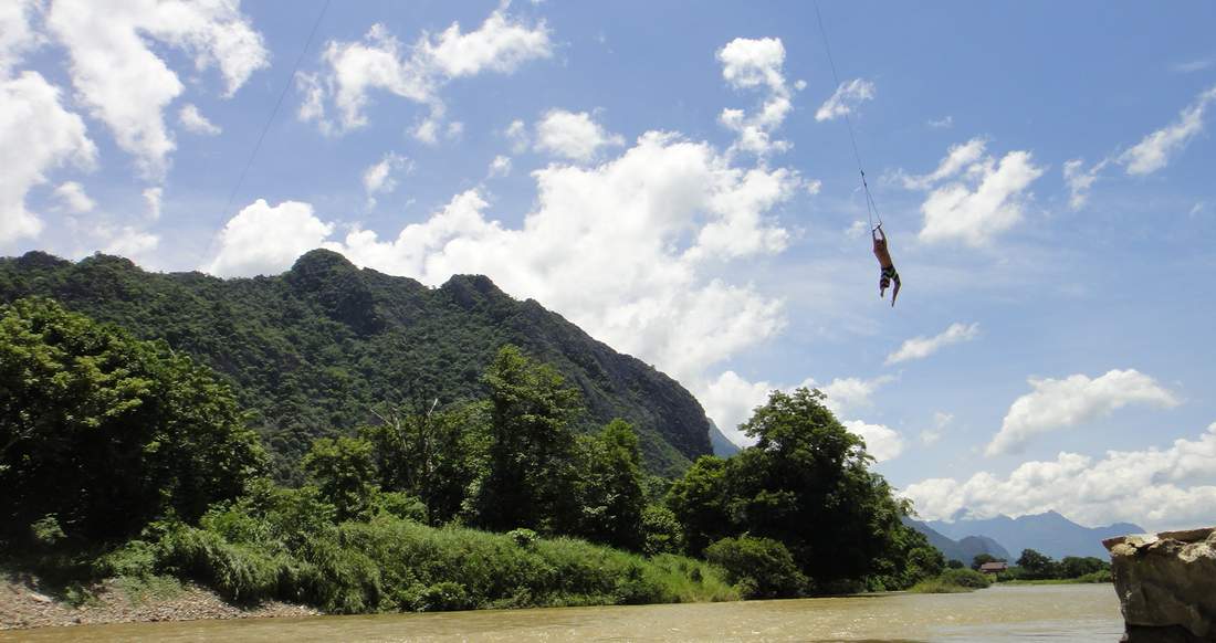 Traveler swinging into the water A man swings into the river in Laos