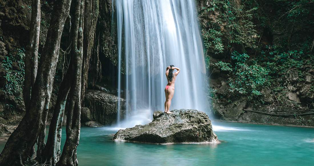 Waterfall in Kanchanaburi Thailand A girl standing in front of a stunning waterfall in Kanchanaburi Thailand